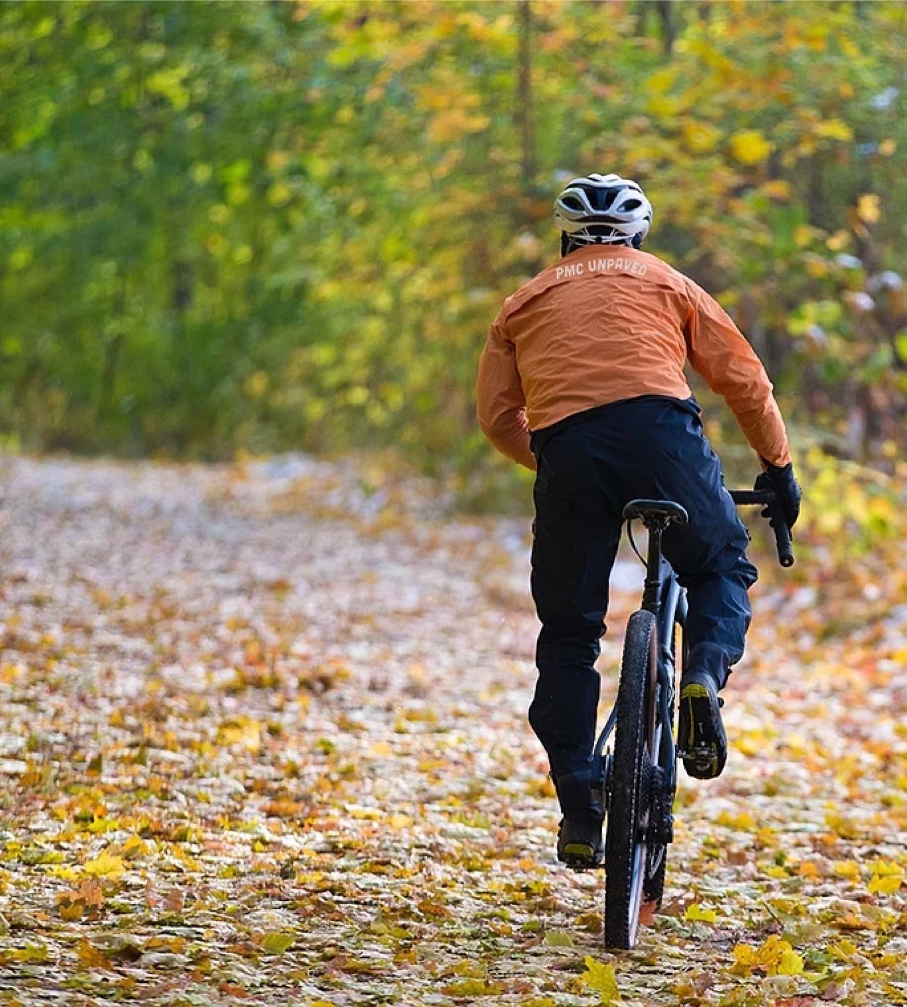 Cyclist with an orange jacket riding through a leaf covered path