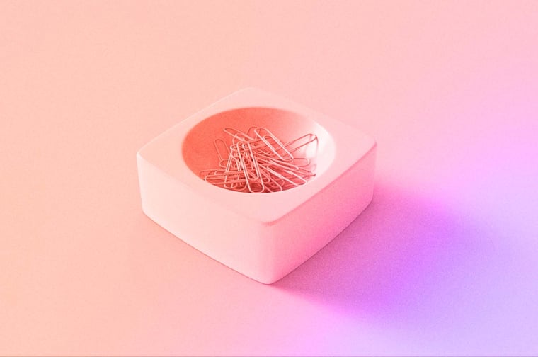 A pink dish full of paper clips. 