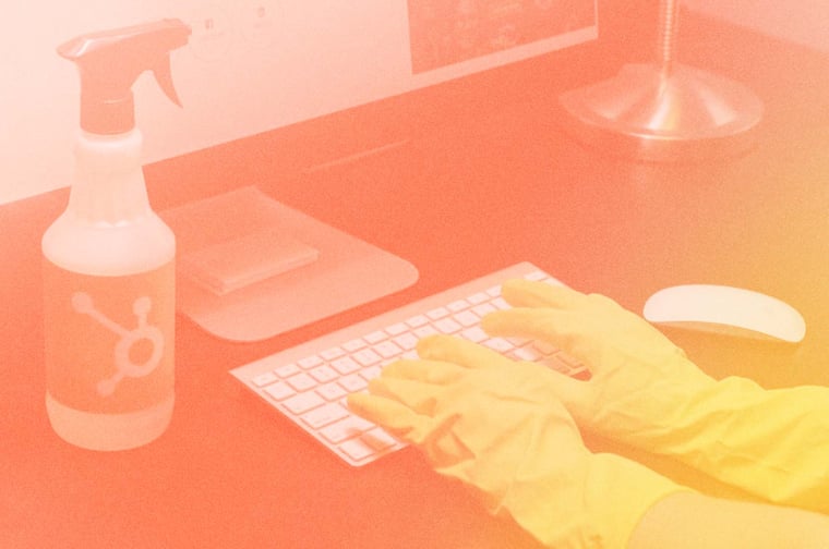 Cleaning materials near computer with person using gloves on the keyboard. 