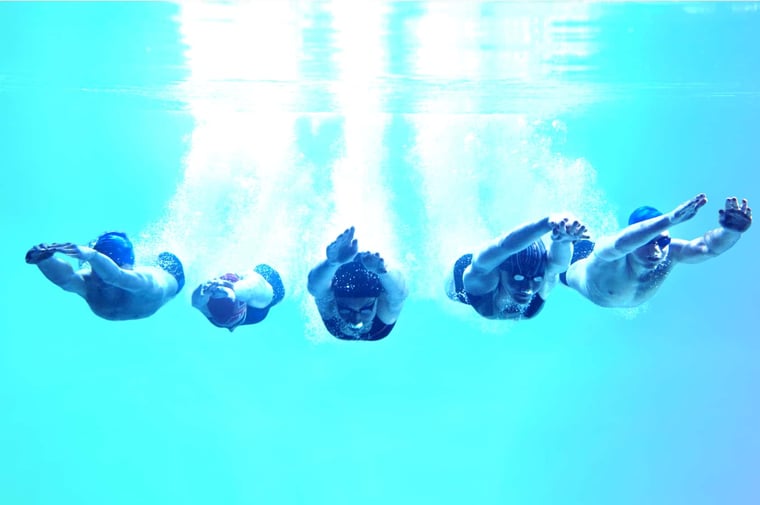 five divers under water swimming towards camera with an aqua gradient background